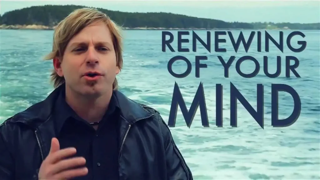 Man speaking in a dark jacket beside a lake with the title 'Renewing of Your Mind' overlaid behind him and water in the background.