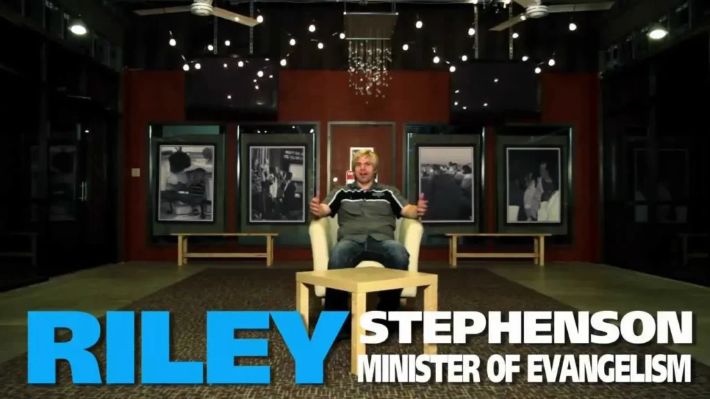 Intro image: man seated in a beige chair in a studio with framed photos on the back wall; large blue text 'RILEY' and white text 'STEPHENSON MINISTER OF EVANGELISM' across the bottom.