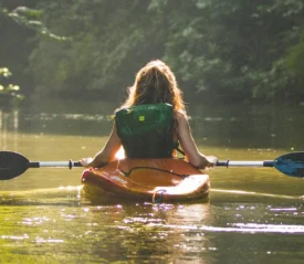 Person kayaking in a body of water holding paddles.