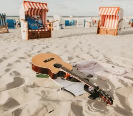 A guitar laying in sand at the beach.