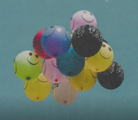 Balloons floating outside with smiley faces on them.