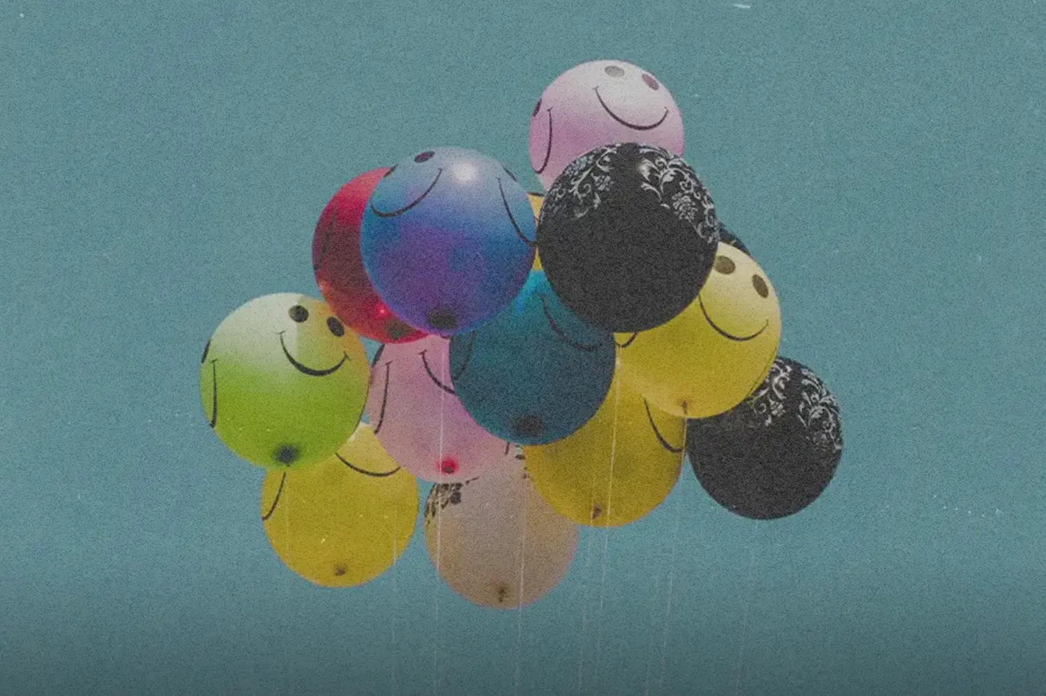 Balloons floating outside with smiley faces on them.