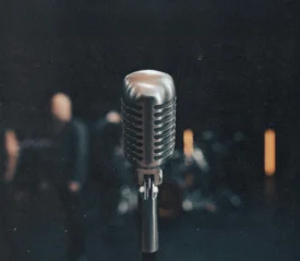 Vintage-style microphone in sharp focus on a dimly lit stage with blurred figures and lights in the background