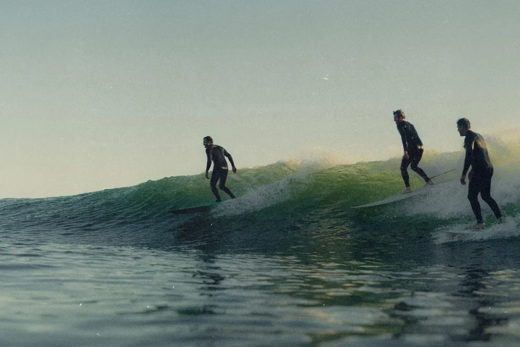 Three surfers ride a green ocean wave together in the soft light of early morning or late afternoon