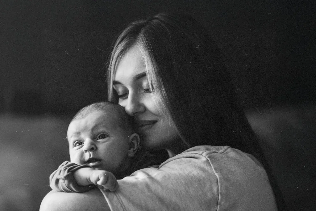 Woman holds a small baby close against her shoulder in a quiet, softly lit setting