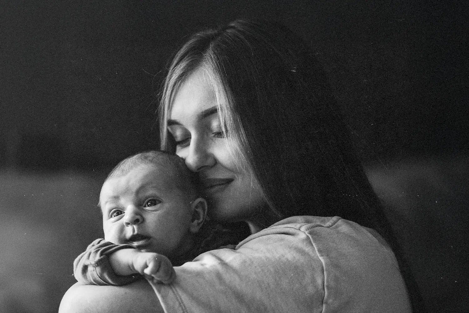 Woman holds a small baby close against her shoulder in a quiet, softly lit setting