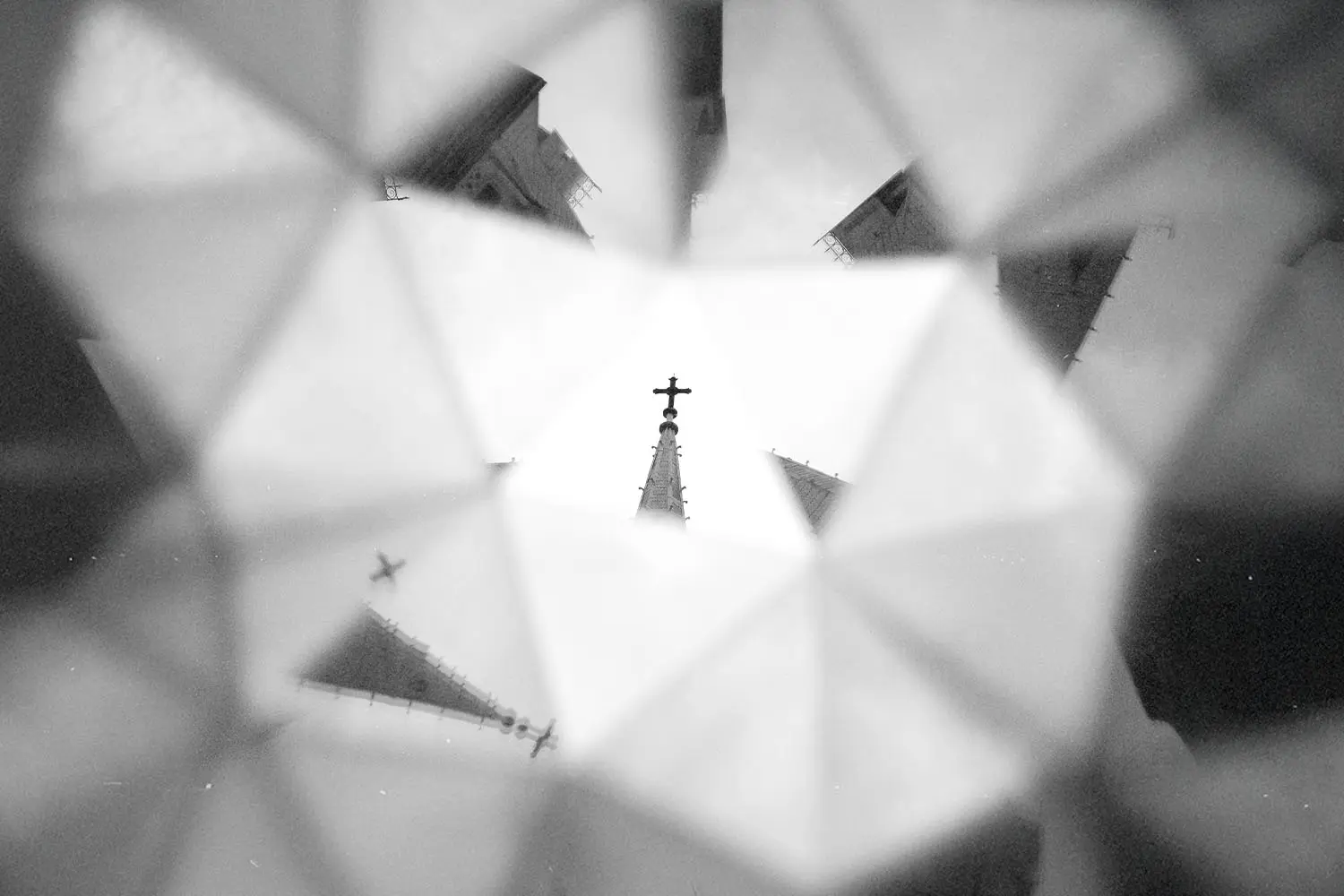 A church steeple topped with a cross is reflected and multiplied through a kaleidoscope‑like pattern of geometric shapes
