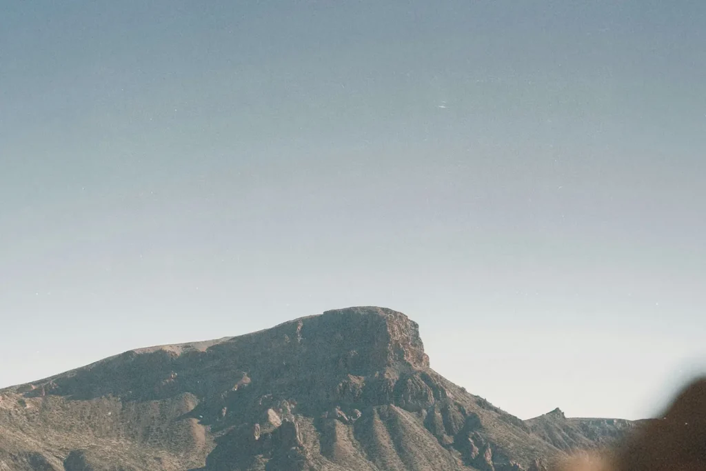 A wide, sunlit mountain ridge rises beneath a clear blue sky