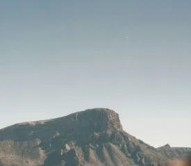 A wide, sunlit mountain ridge rises beneath a clear blue sky