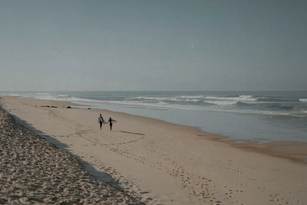 Couple walking along an empty sandy beach beside gentle ocean waves