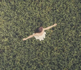 Woman standing with open arms in the middle of a lush green field, viewed from above