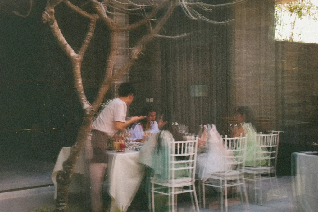Server attending to a group of people dining at an outdoor restaurant, seen through a glass window with soft motion blur