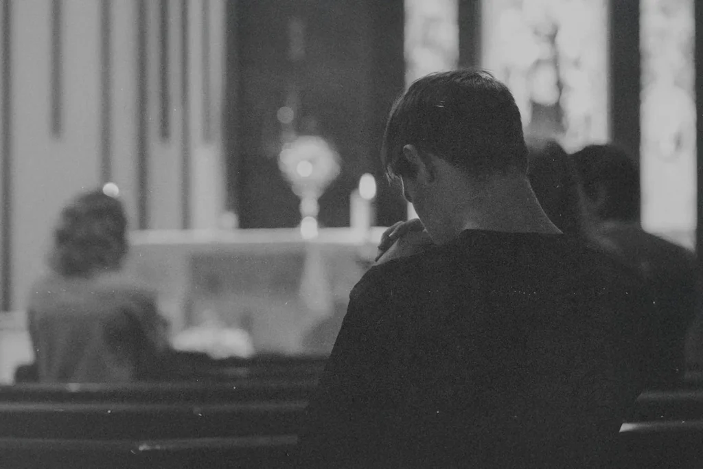 A dimly lit interior of a church where a person sits in a pew facing the altar