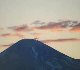 Snow‑covered mountain peak at sunrise with soft pink clouds drifting across the sky