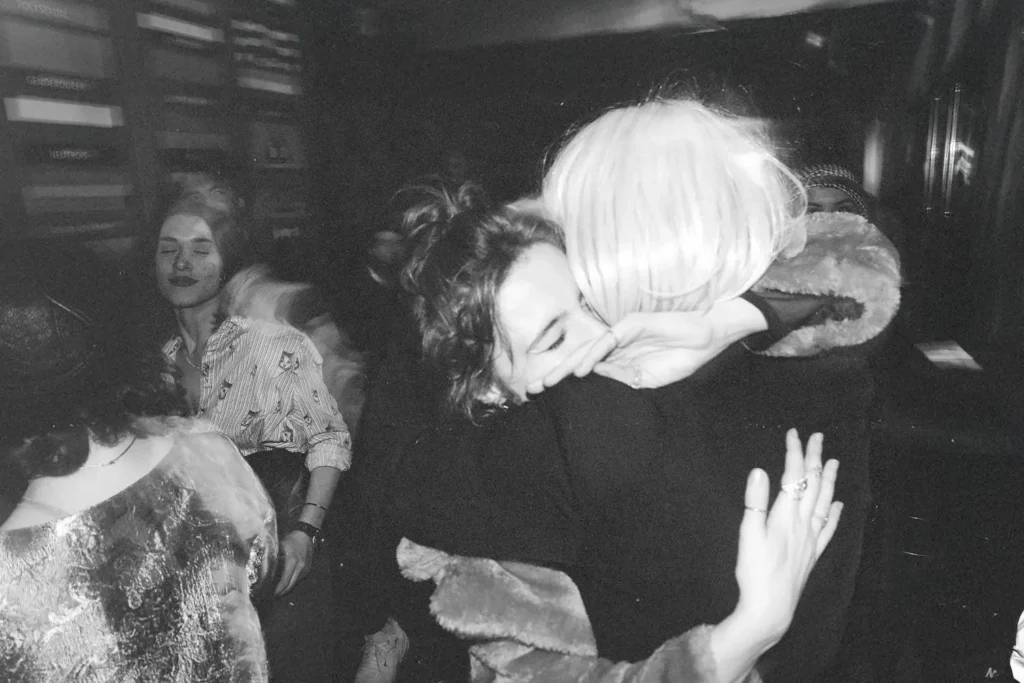 Candid moment of two individuals hugging in a busy room with soft lighting