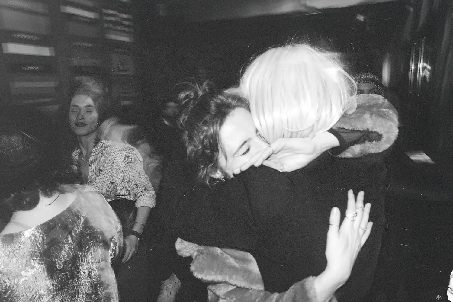 Candid moment of two individuals hugging in a busy room with soft lighting