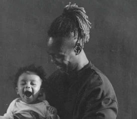 A man smiles while holding a small child in his arms in a softly lit, monochrome portrait