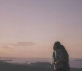 Couple standing arm in arm overlooking a calm lake and distant hills at sunset