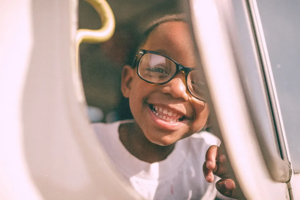 A child sits by a window on a vehicle, resting a hand on the window frame while looking outside