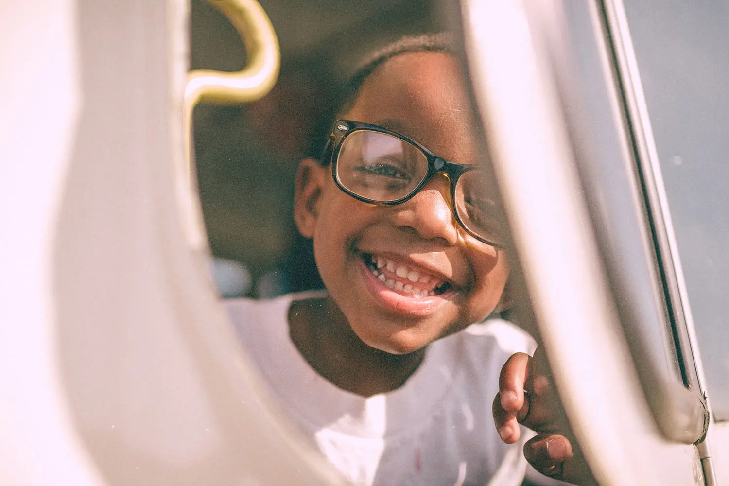 A child sits by a window on a vehicle, resting a hand on the window frame while looking outside