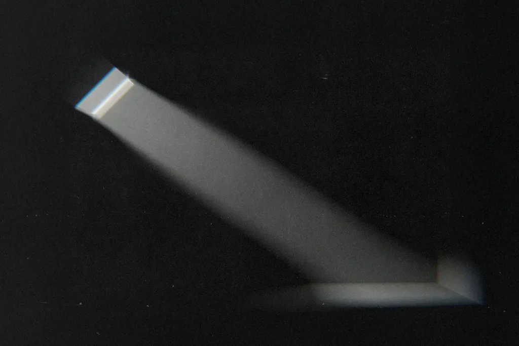 A narrow beam of light shines through a small window or opening, cutting across a dark room and illuminating a portion of the wall and floor