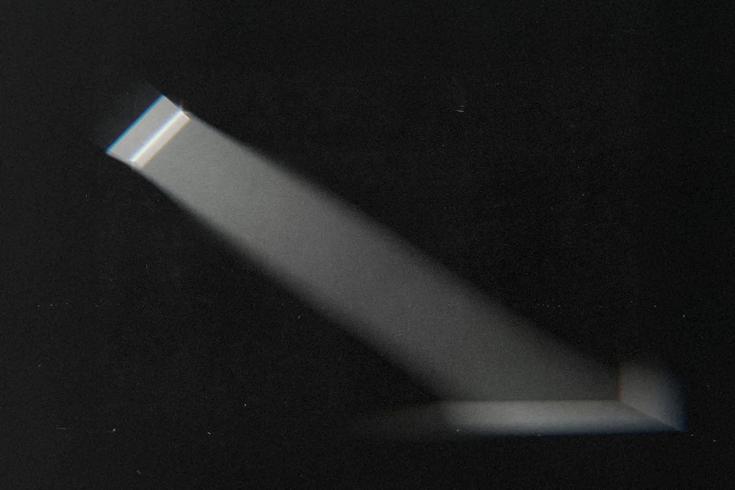 A narrow beam of light shines through a small window or opening, cutting across a dark room and illuminating a portion of the wall and floor