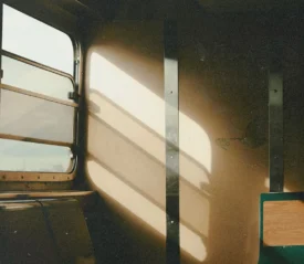 Warm sunlight streams through the window of an old train car, casting long, soft shadows across the beige interior walls and empty seats