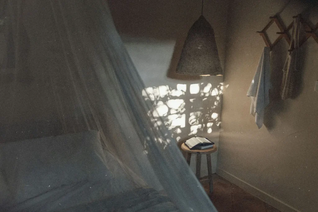 Soft morning light filters through a window into a cozy bedroom, illuminating an open book on a small wooden stool