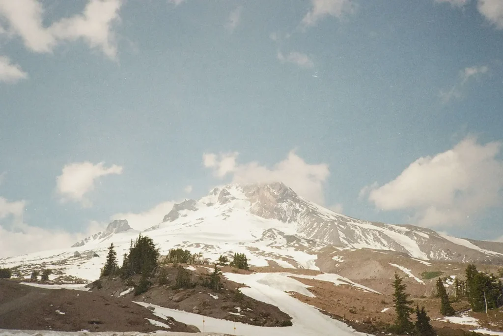 A snow‑covered mountain rises beneath a bright blue sky with scattered white clouds