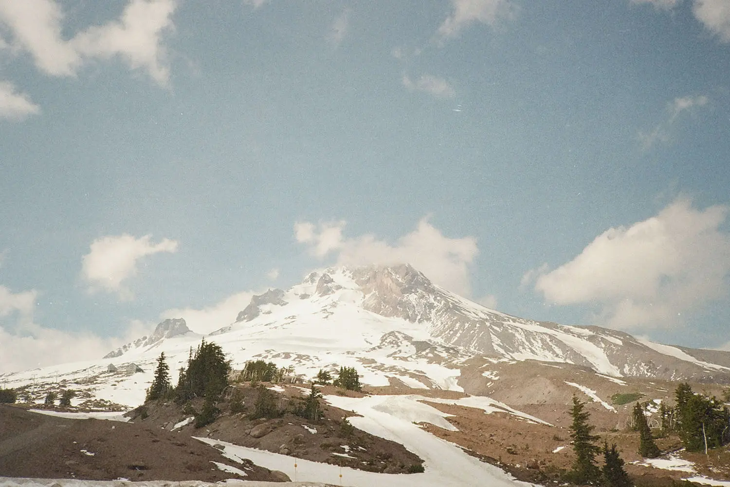 A snow‑covered mountain rises beneath a bright blue sky with scattered white clouds