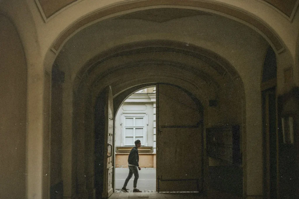 A person walks through a large arched doorway into a quiet courtyard, framed by the tall curved entryway