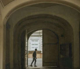 A person walks through a large arched doorway into a quiet courtyard, framed by the tall curved entryway