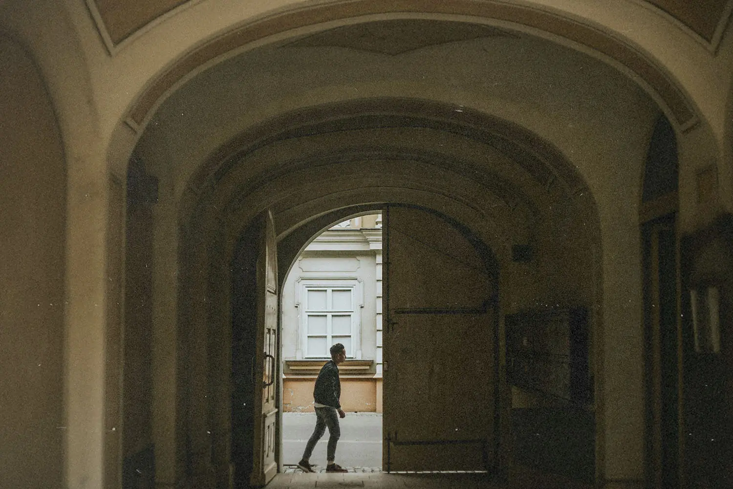 A person walks through a large arched doorway into a quiet courtyard, framed by the tall curved entryway