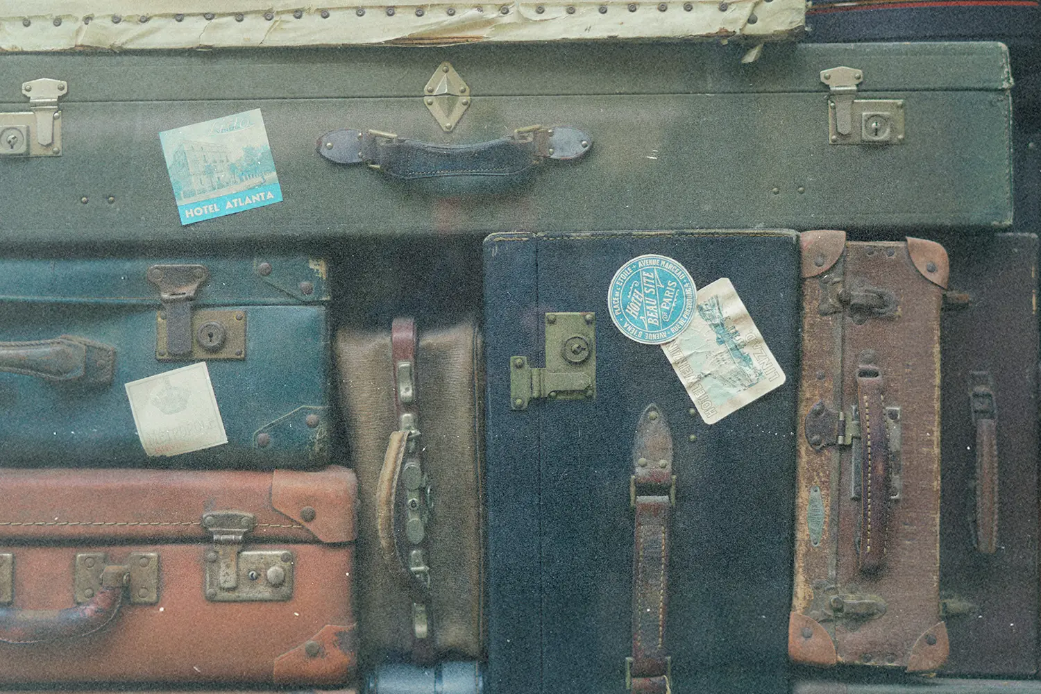Collection of old-fashioned suitcases stacked tightly together, some decorated with vintage travel stickers