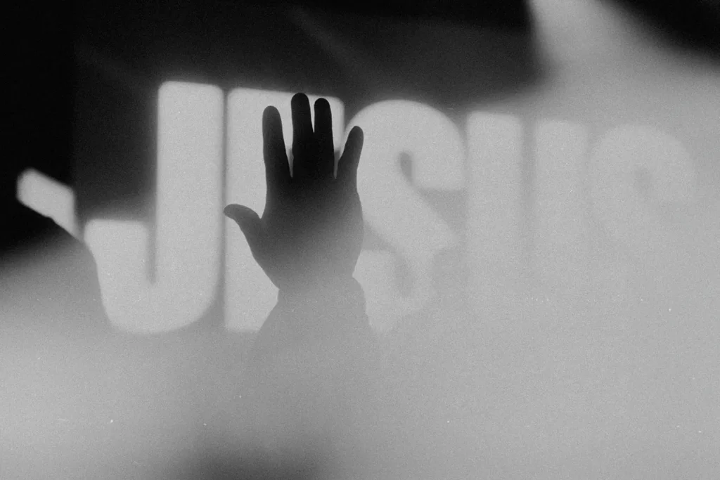 Silhouetted hand raised toward an illuminated screen with "Jesus" in bold text in the background