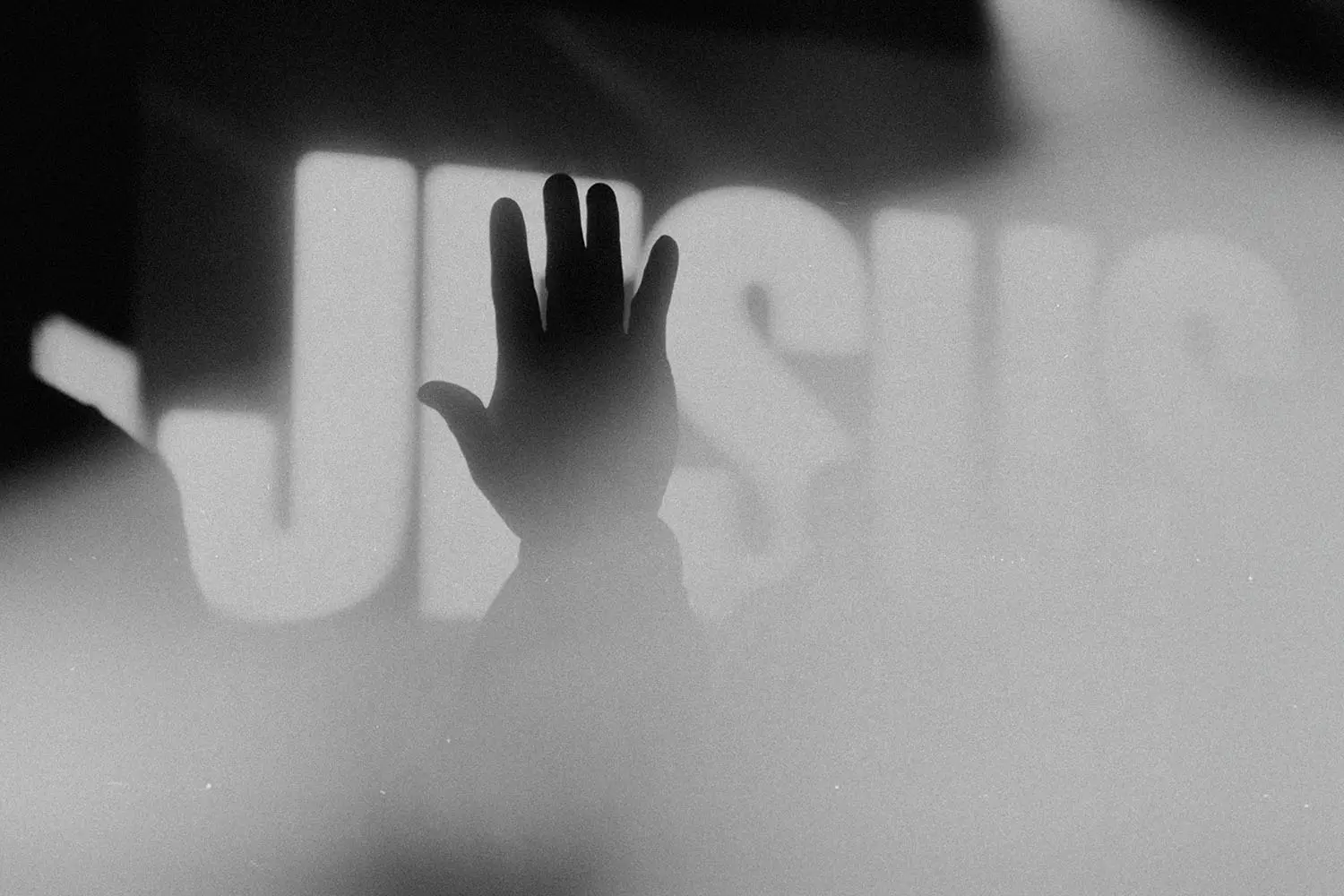 Silhouetted hand raised toward an illuminated screen with "Jesus" in bold text in the background