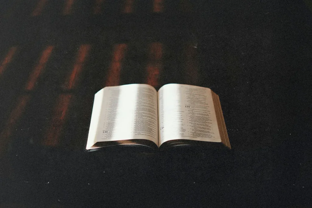 An open Bible rests on a dark surface with warm light softly illuminating the pages