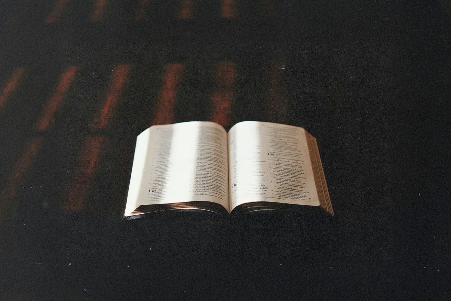 An open Bible rests on a dark surface with warm light softly illuminating the pages