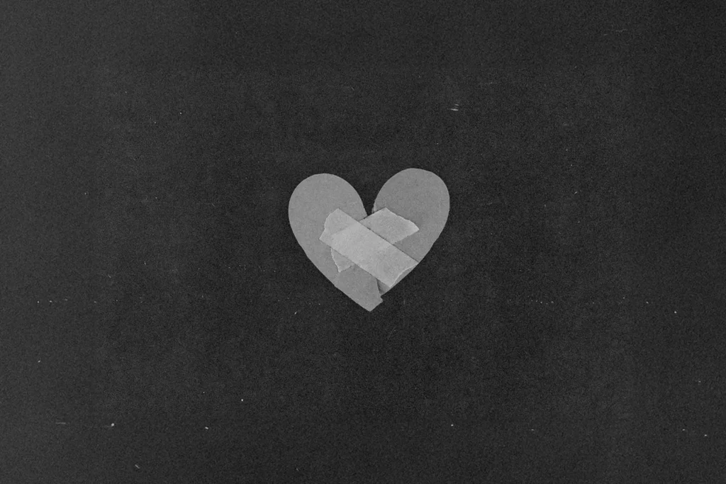 A simple paper heart sits against a dark background with two pieces of tape placed in an “X” shape across the center