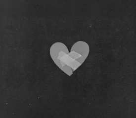 A simple paper heart sits against a dark background with two pieces of tape placed in an “X” shape across the center