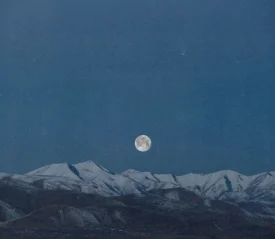 Full moon rising above a snow‑covered mountain range under a deep blue sky