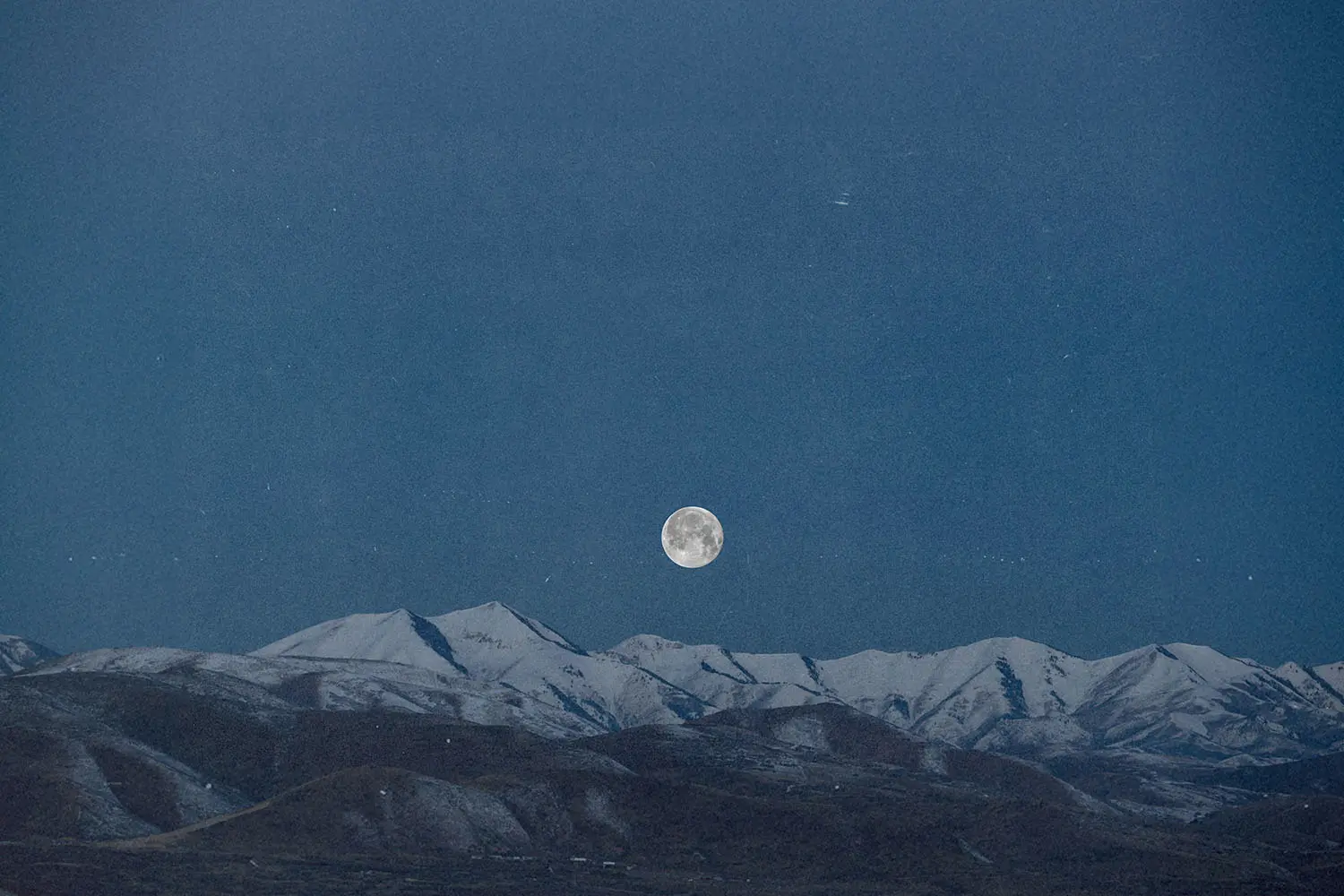 Full moon rising above a snow‑covered mountain range under a deep blue sky