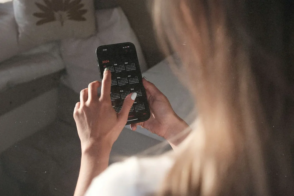 A person uses a smartphone, tapping on a full-year calendar displayed on the screen