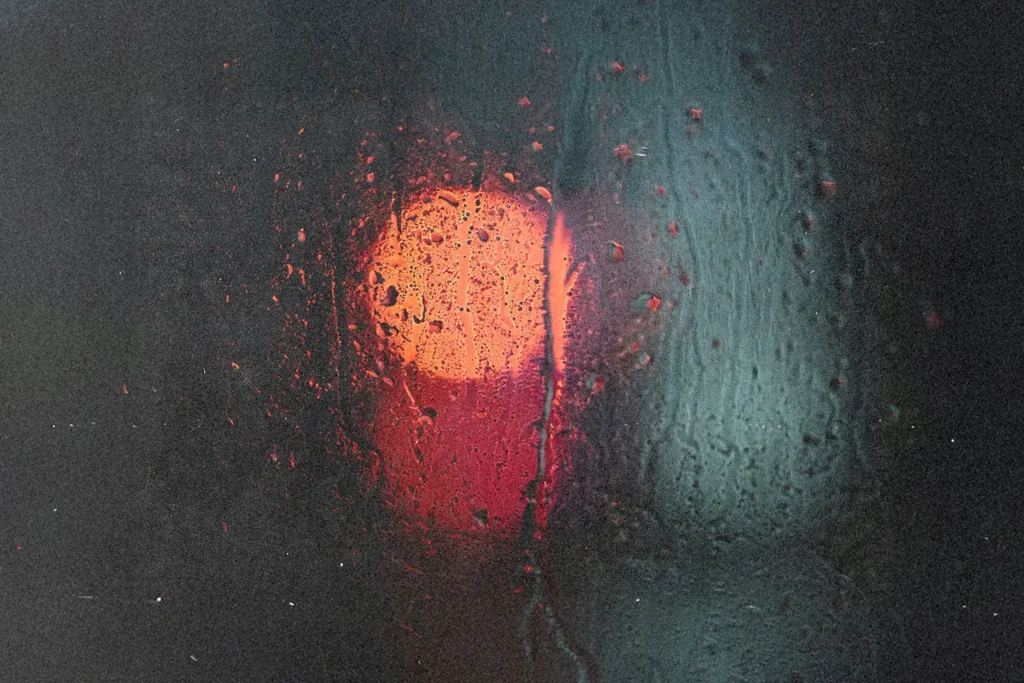 Blurred red and blue lights shining through a rain‑covered window