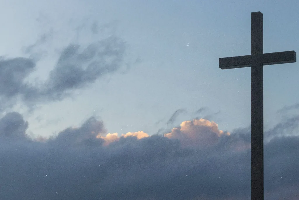 A large cross silhouetted against a cloudy sky with soft light breaking through