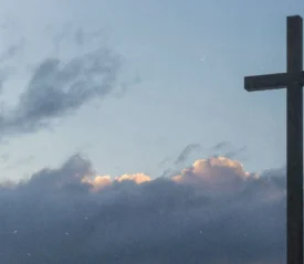 A large cross silhouetted against a cloudy sky with soft light breaking through