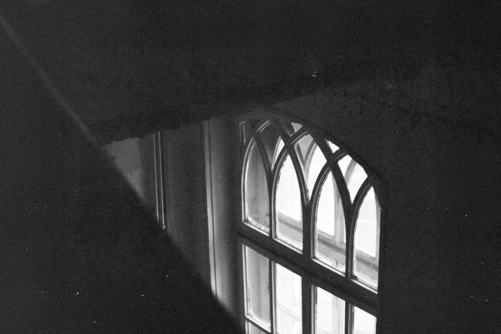 A softly lit arched window seen from above in a dark interior, with faint light shining through the glass panes