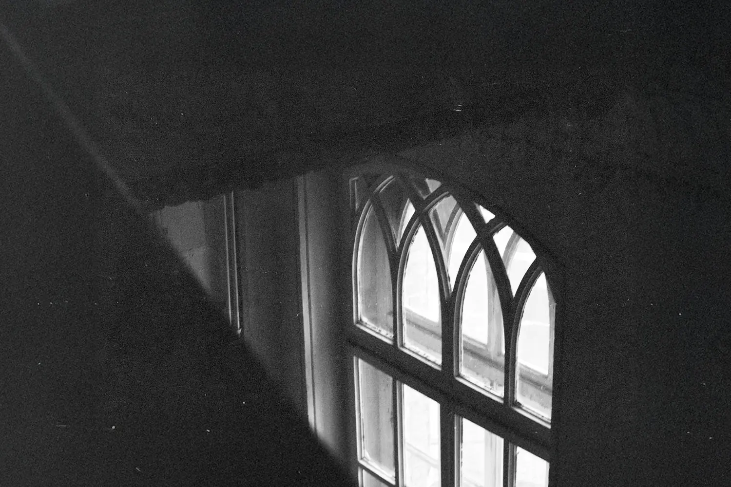 A softly lit arched window seen from above in a dark interior, with faint light shining through the glass panes