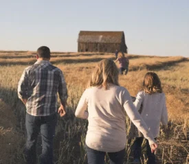 Group of people walking through a golden field toward an old wooden barn under a clear blue sky