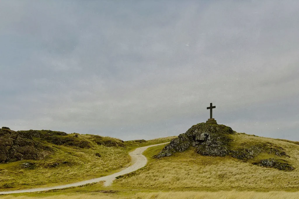 Hilltop cross rising above rolling grasslands beneath an overcast sky